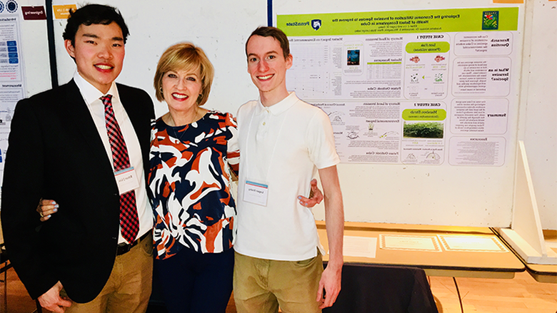 two male students and female professor in front of poster presentation