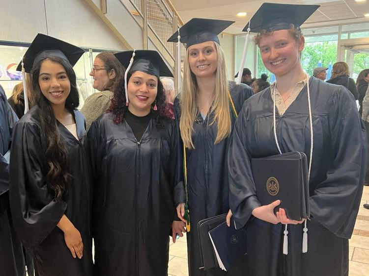 四名毕业生在毕业典礼上戴着帽子，穿着礼服摆姿势拍照